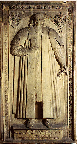 Ein aus Sandstein gefertigtes Relief, auf dem eine männliche Person in langem Mantel dargestellt ist.