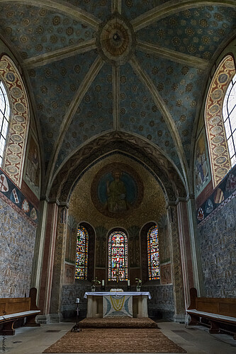 Ein moderner Alta, dahinter sind drei Buntglasfenster zu sehen, die Gewölbedecke ist mit aufwändigen Malereien geschmückt.