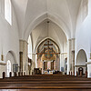 Romanischer Kirchinnenraum mit hellen Wänden und Fenstern in Rundbögen.