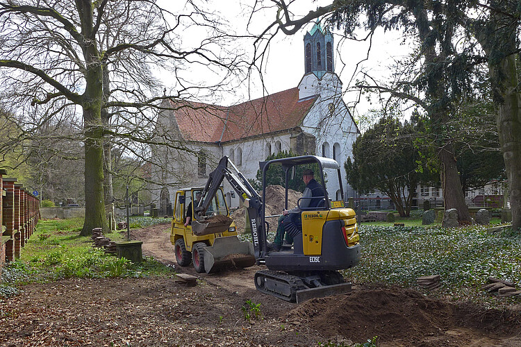 Zwei Baumaschinen arbeiten an einer Fläche, die zum Friedhof gehört, vor der Kirche Marienwerder.