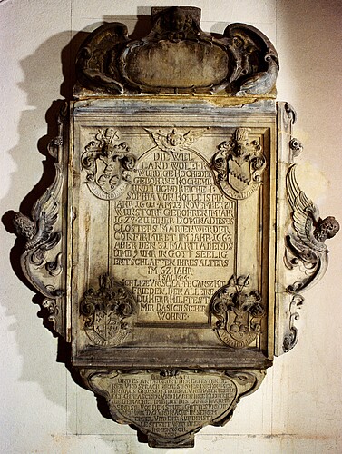 Ein aus Stein gefertigtes Relief mit einer Inschrift und schmückenden Verzierungen.
