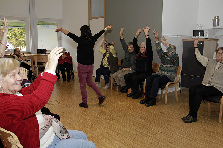 Eine Reihe von Seniorinnen und Senioren sitzt in einem Stulhkreis und macht gemeinsam Übungen.