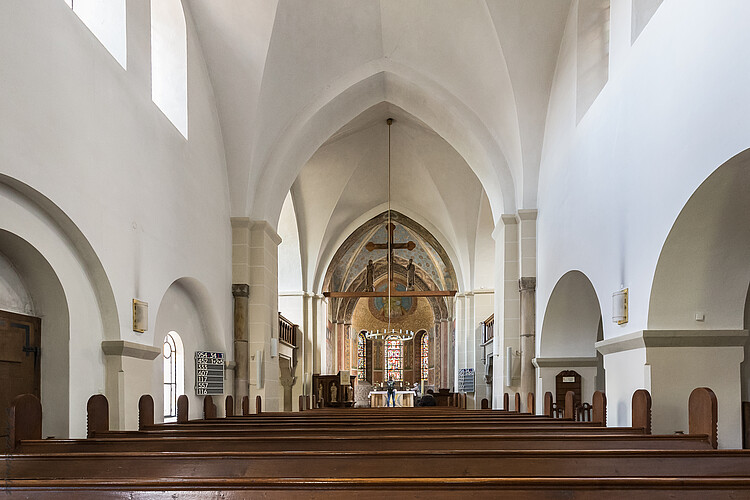 Romanischer Kirchinnenraum mit hellen Wänden und Fenstern in Rundbögen.